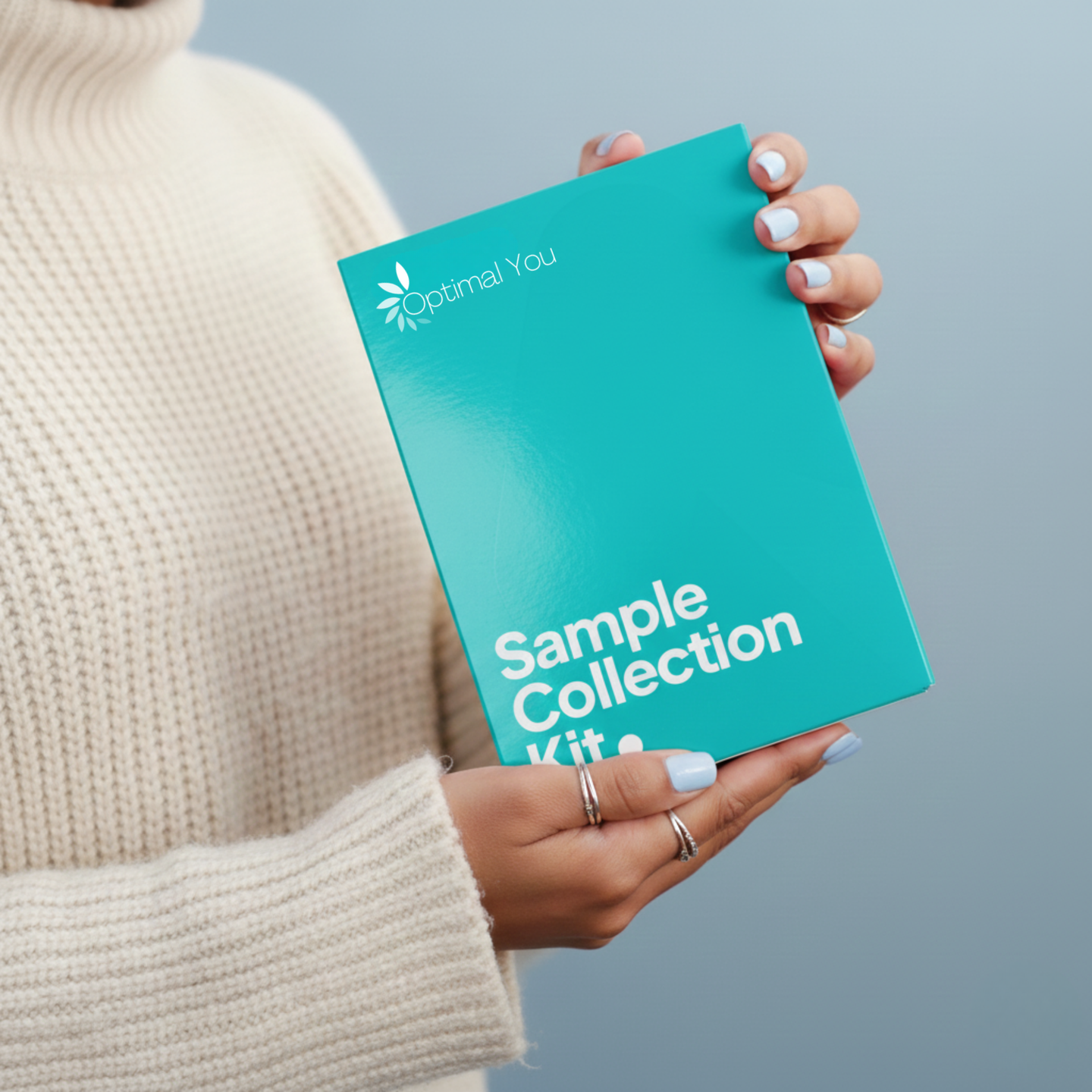 Person holding a teal 'Optimal You' sample collection kit against a light blue background wearing rings